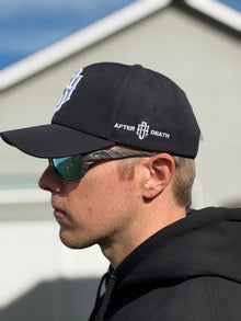 Person wearing a black cap with 'After Death' logo and sunglasses, standing outdoors.
